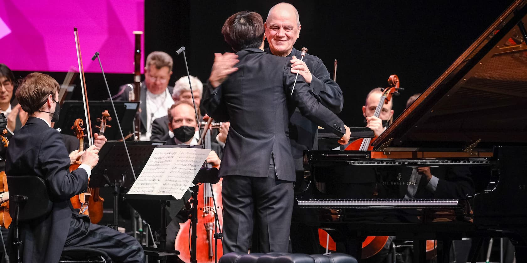 Conductor hugs pianist on stage while the orchestra plays.