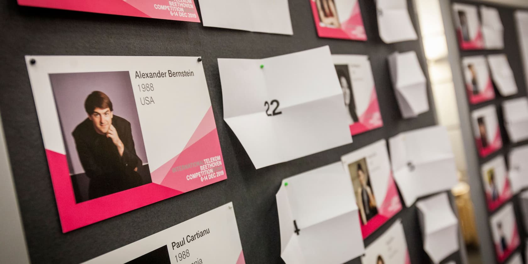 A bulletin board with participant photos and name tags for the International Telekom Beethoven Competition 2019. One name tag shows Alexander Bernstein, 1988, USA.