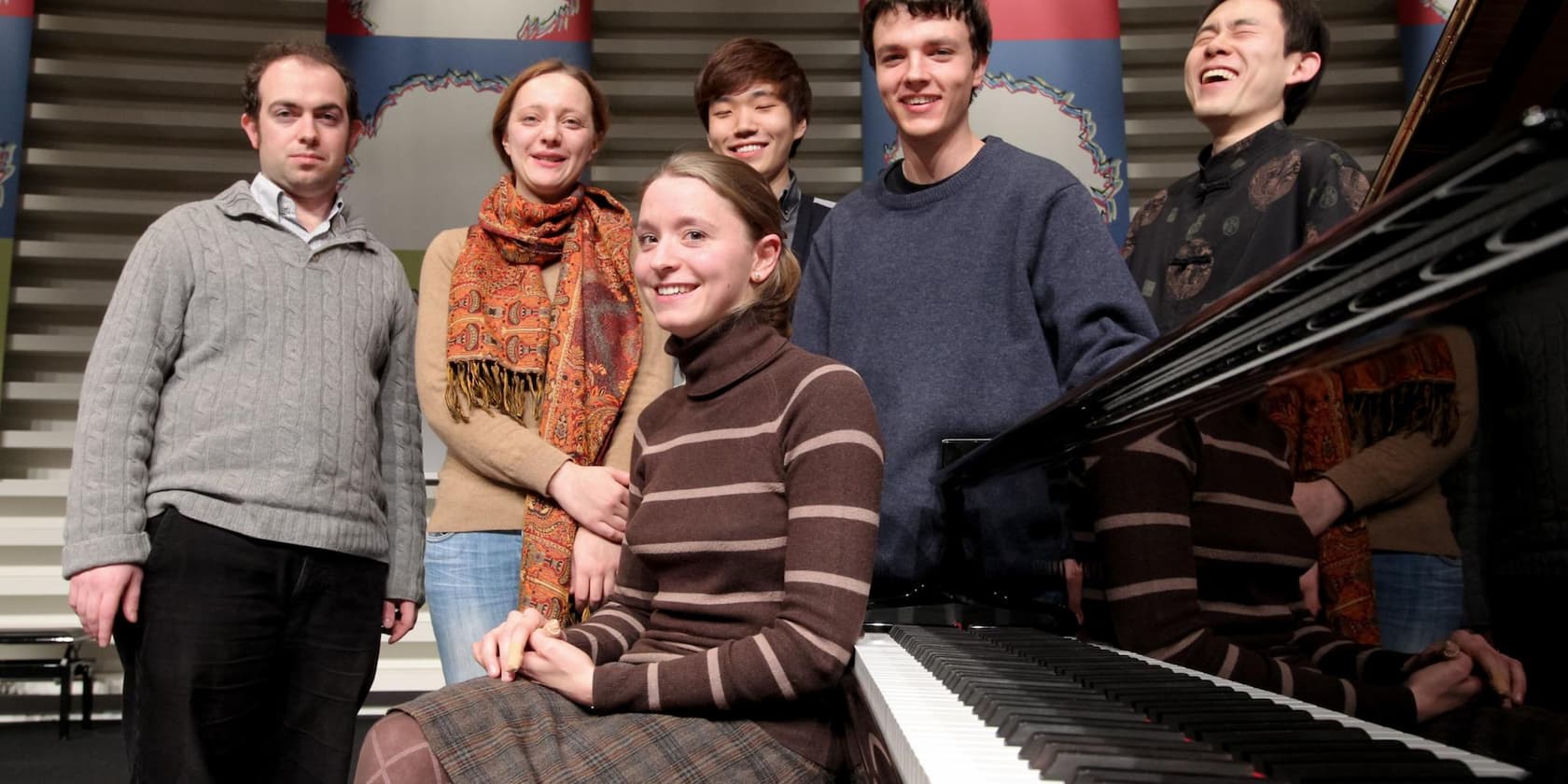 Gruppe von fünf Personen, mit einer Frau im Vordergrund an einem Klavier.