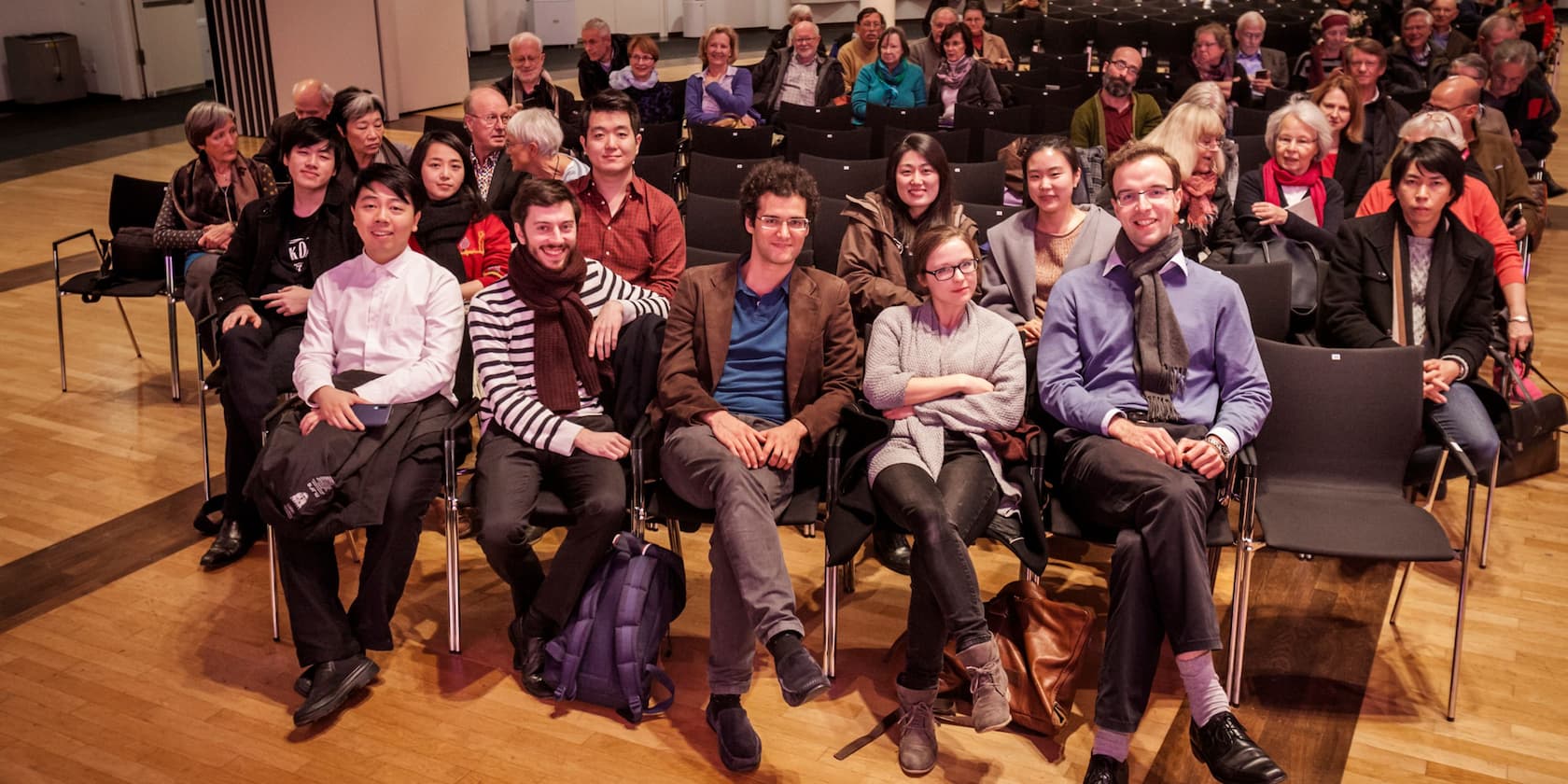 Eine Gruppe von Menschen sitzt in einem Auditorium und lächelt in die Kamera.