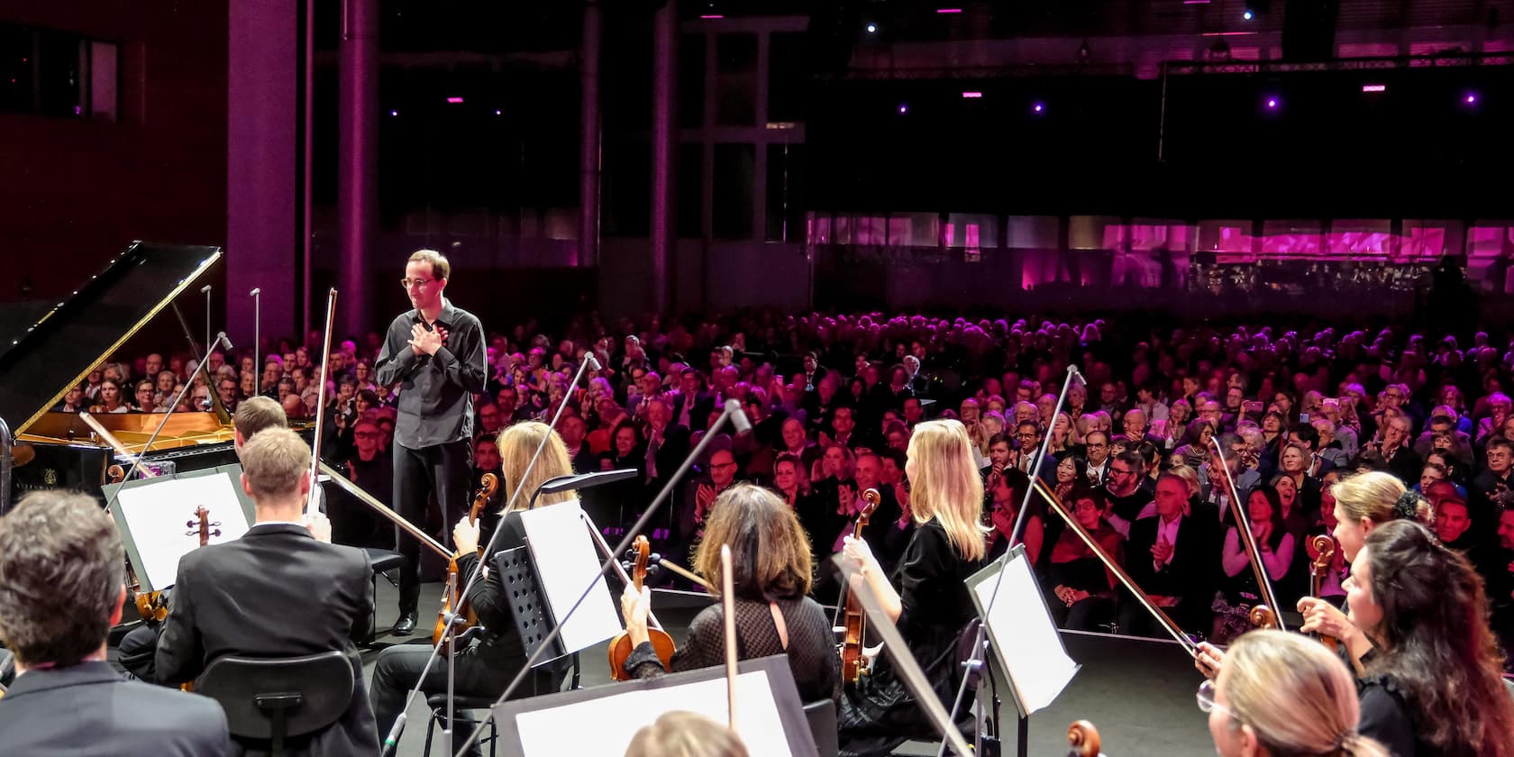 Conductor and orchestra in front of an audience in a concert hall.