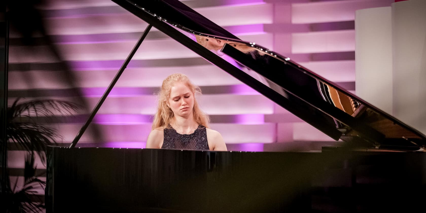 A woman plays piano in a room with purple lighting.