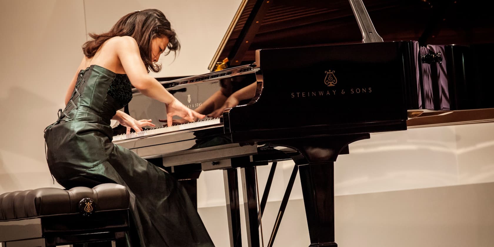 A woman in a green dress playing a black Steinway & Sons piano.