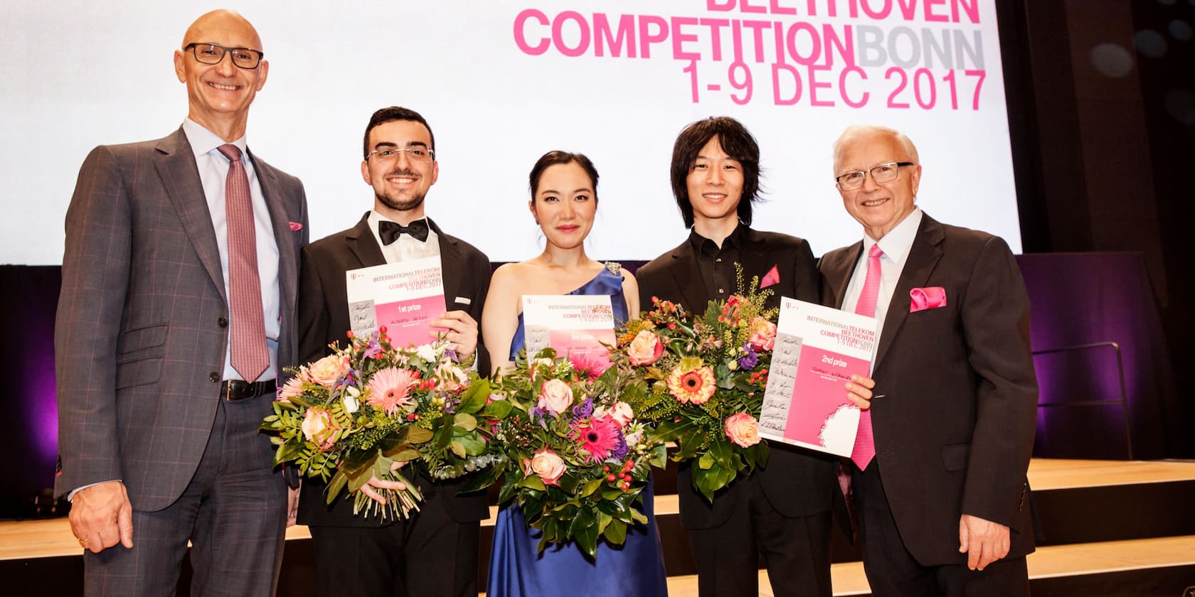 Gruppenfoto von fünf Personen bei der Beethoven-Wettbewerb Bonn, die Preisdokumente und Blumensträuße halten. Text im Hintergrund: 'Beethoven Competition Bonn 1-9 Dec 2017'.