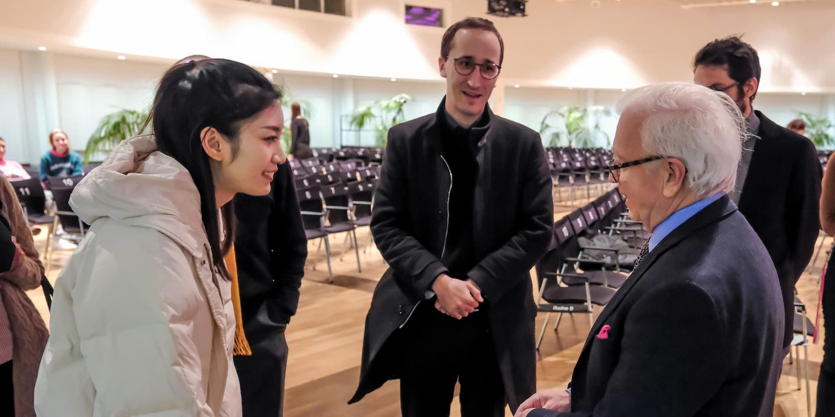 People talking in a hall with empty rows of chairs in the background.