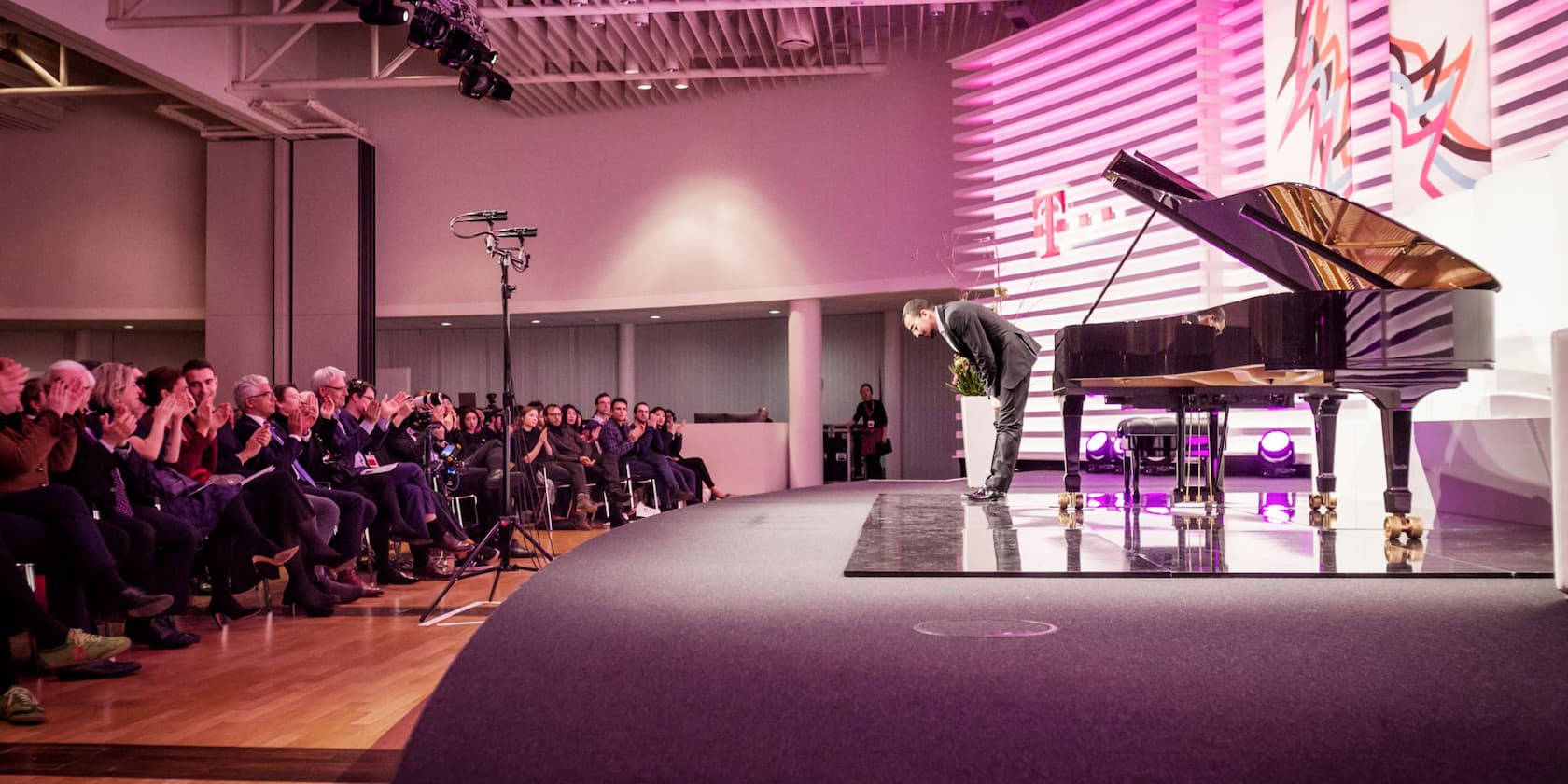 A pianist bows to an applauding audience after a concert. A grand piano is on the stage.