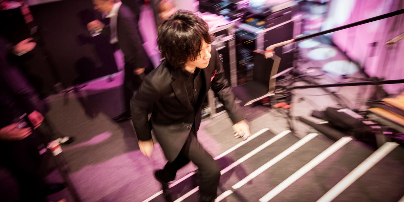 A person in a black suit runs up stairs at an event with purple lighting.