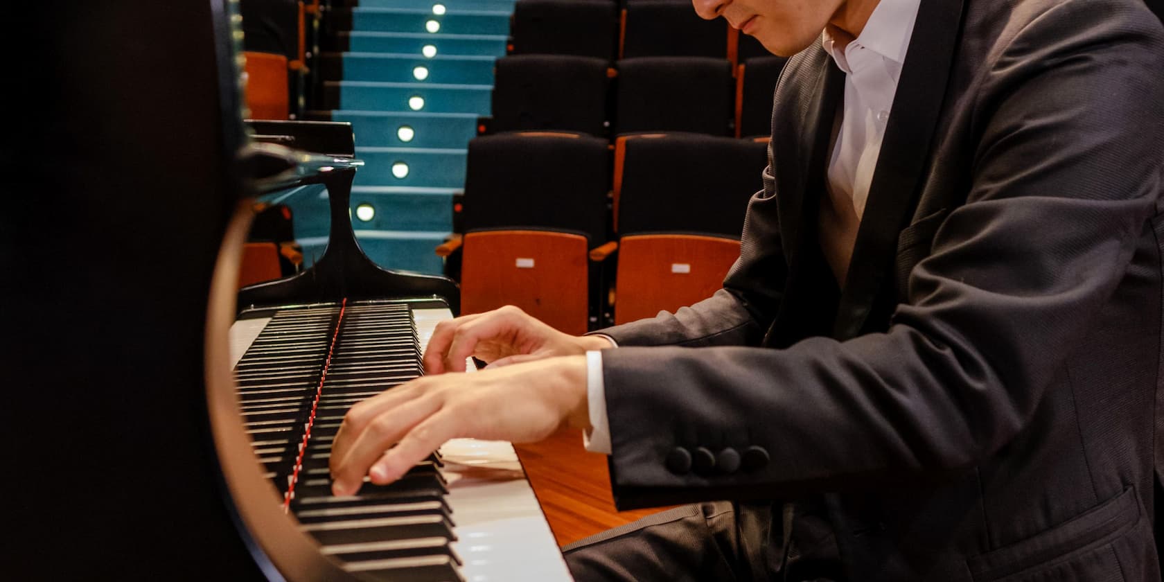 Person spielt Klavier in einem Konzerthallenraum.