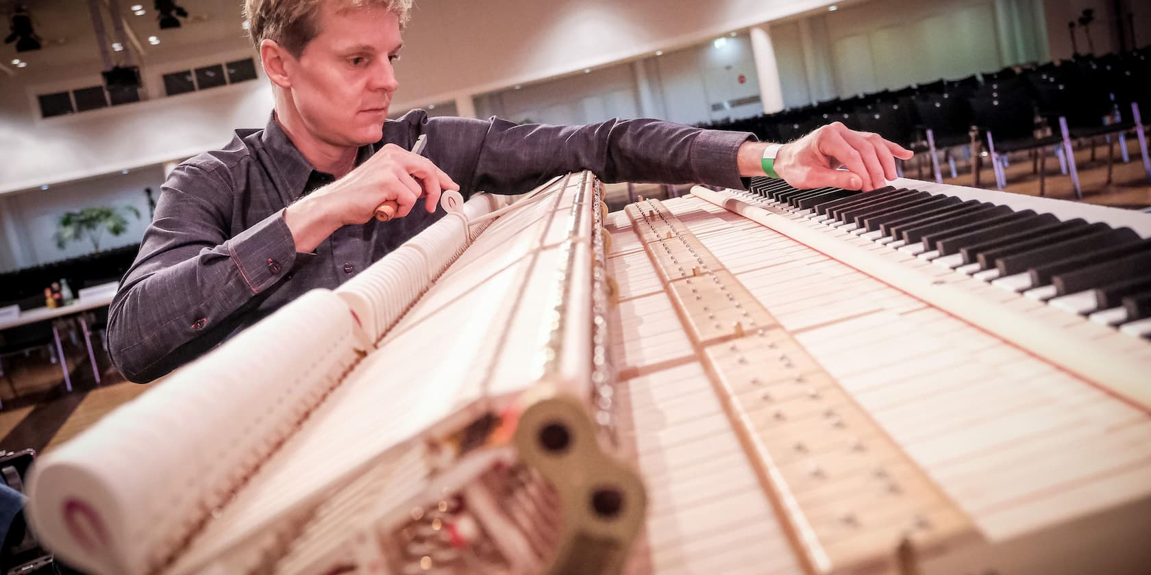 A man tuning a piano in an empty room.