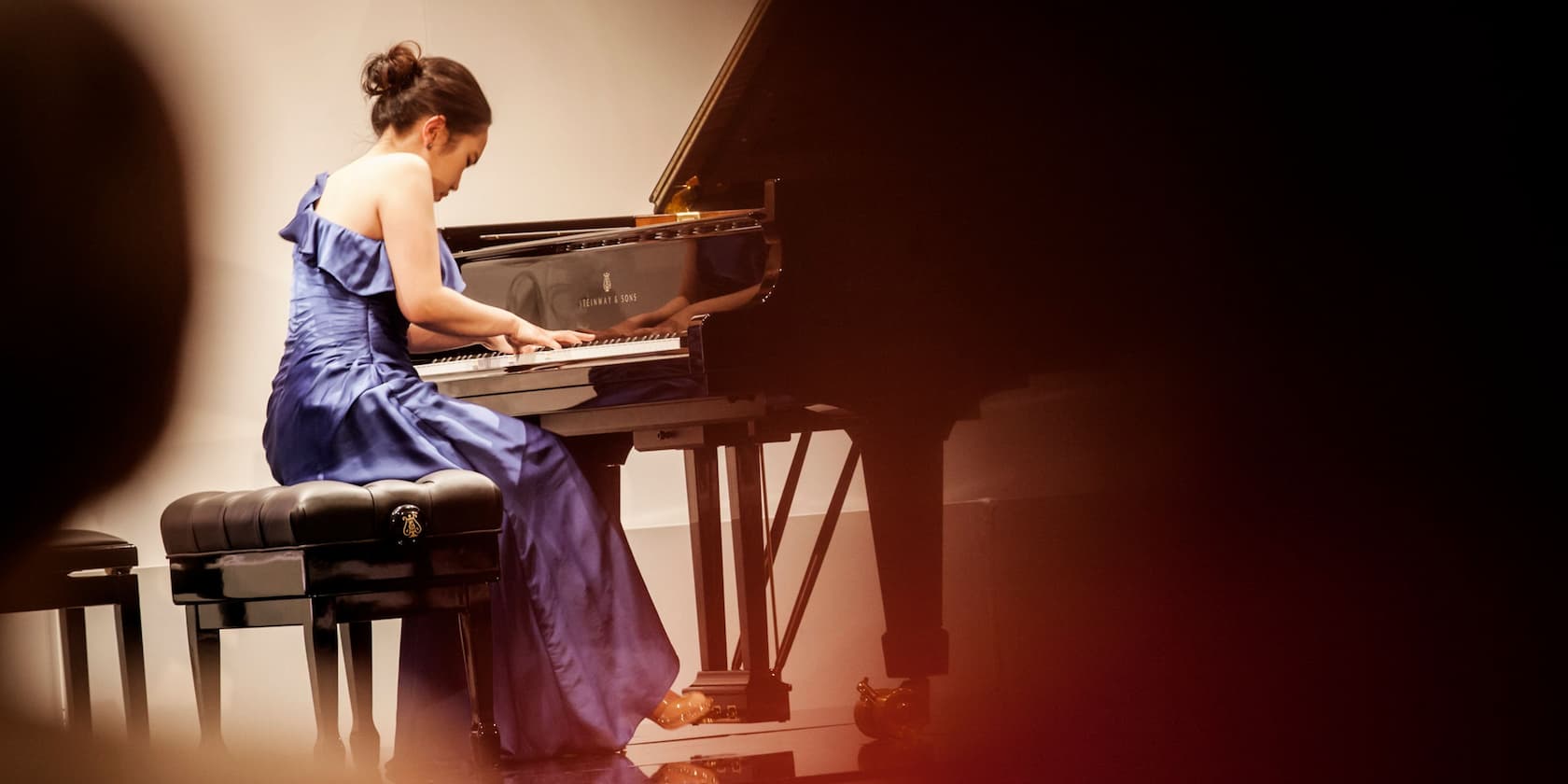 A woman in a blue dress playing the piano at a concert.