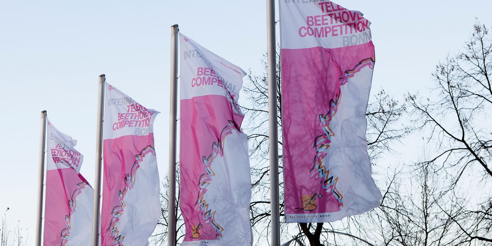 Vier rosa-weiße Fahnen mit der Aufschrift 'International Telekom Beethoven Competition Bonn' wehen im Wind.