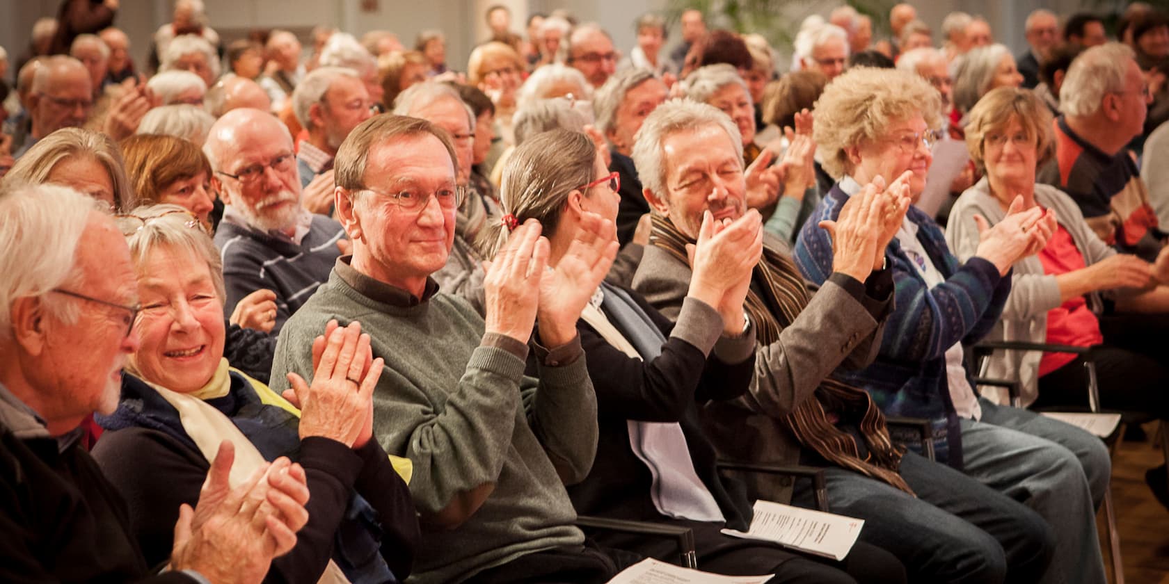 A group of elderly people sitting in an audience and clapping.