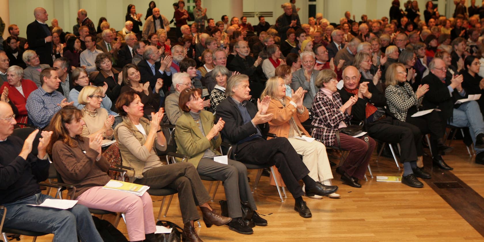 A large group of people is seated in an auditorium, applauding.