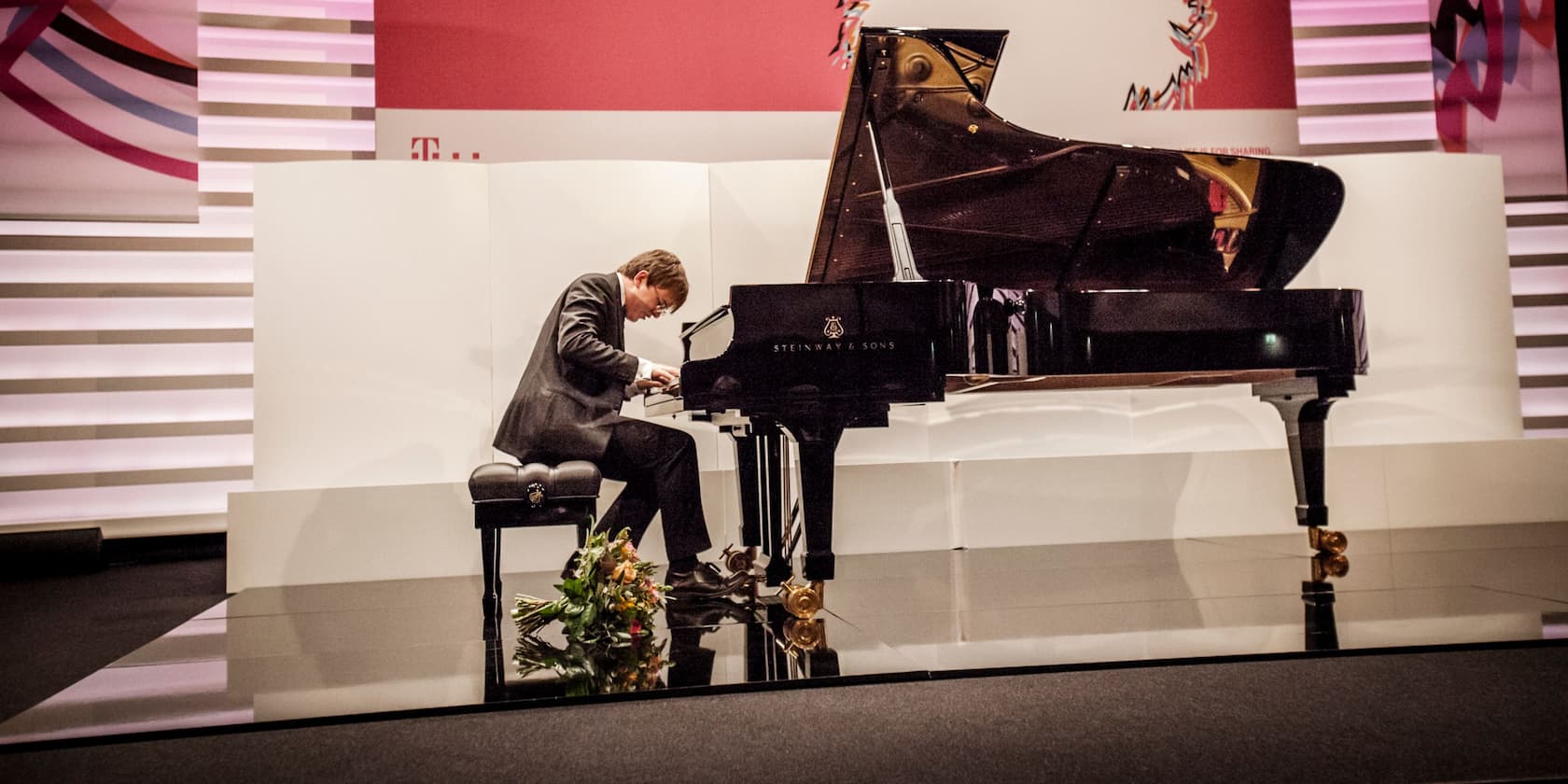 Man playing piano in a concert hall with a bouquet of flowers on the floor.