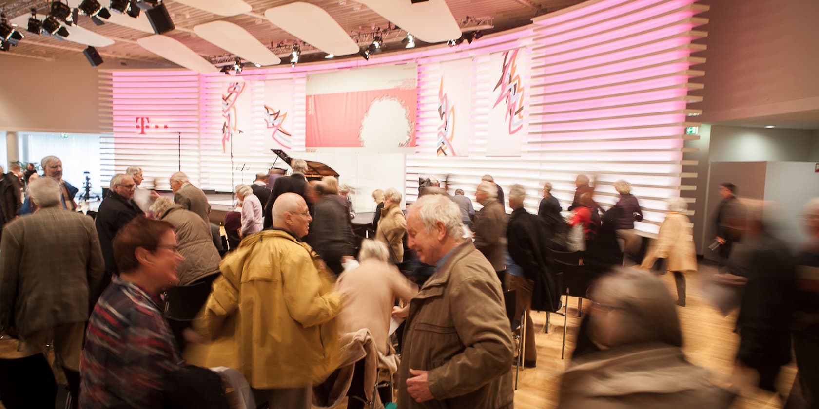 Crowd at an event in a modern hall with a pink-lit background.