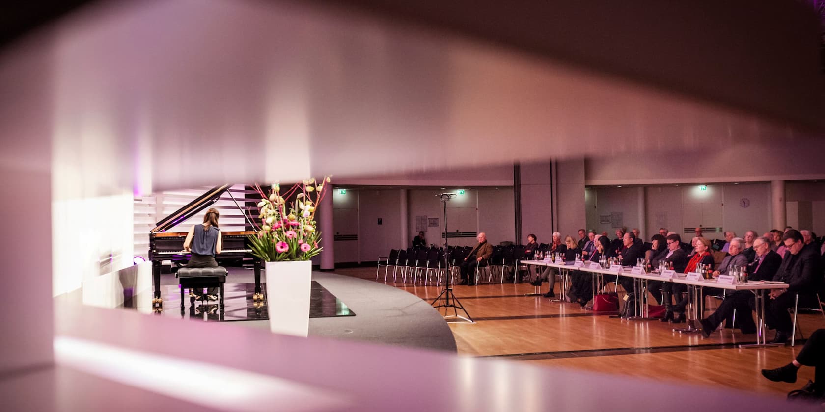 A woman plays the piano in front of an audience in a conference room.