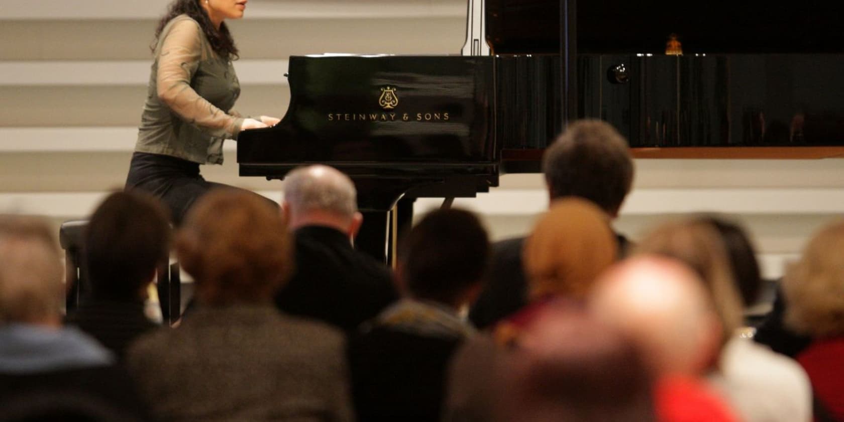 A woman plays a Steinway & Sons grand piano in front of an audience.