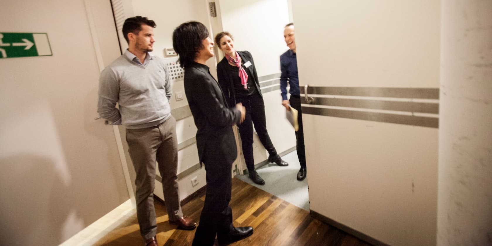 Four people are conversing near an open door indoors.