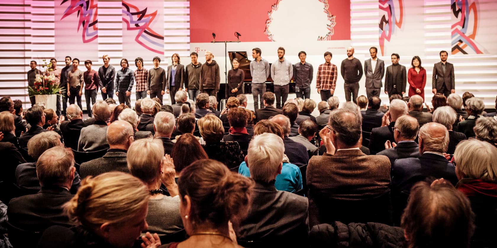 Menschenmenge, die einer Gruppe von Personen auf einer Bühne bei einer Veranstaltung applaudiert.