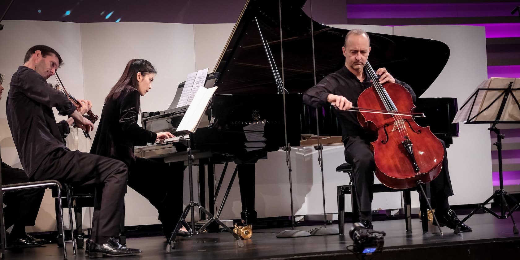 Chamber music trio performs on stage: violinist, pianist, and cellist