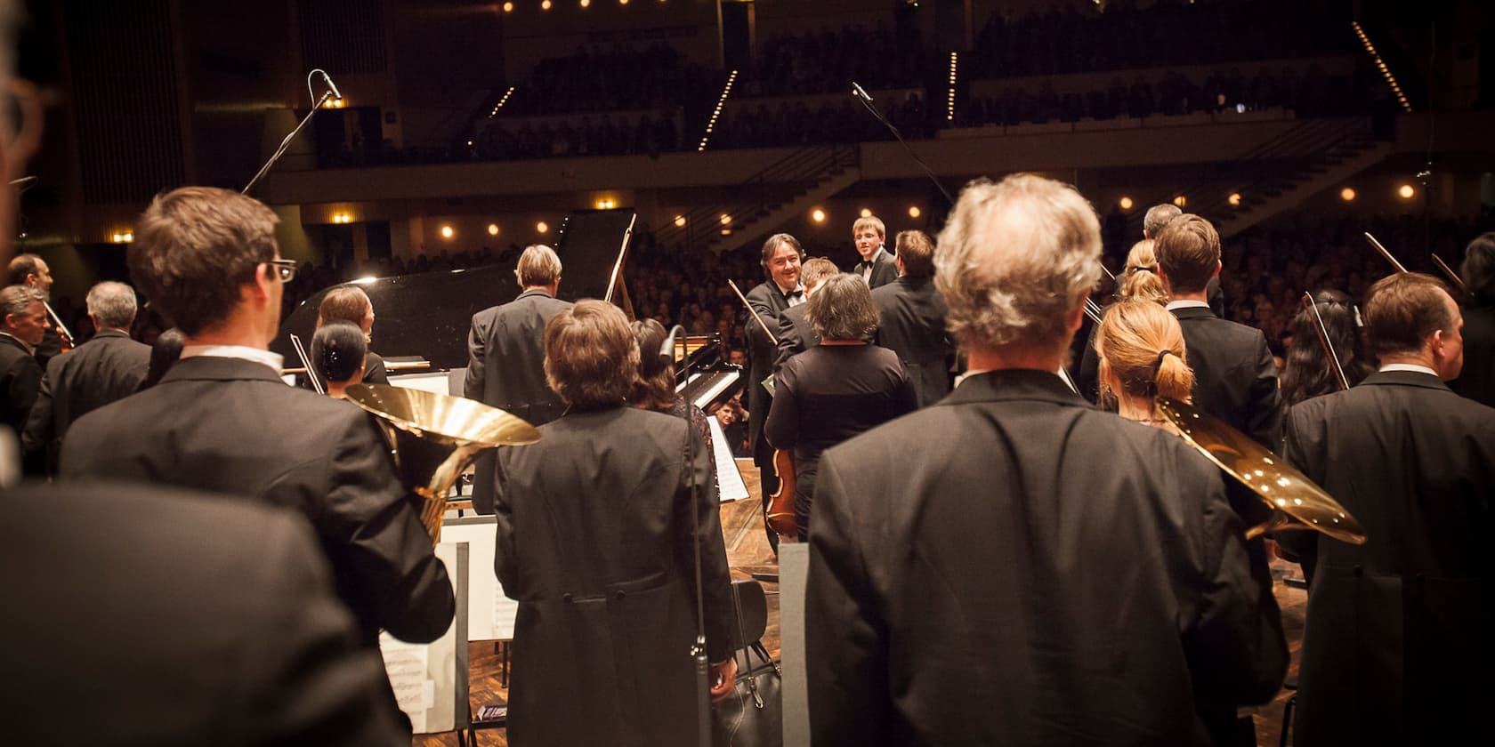 An orchestra prepares for a performance, musicians holding their instruments and standing on a stage.