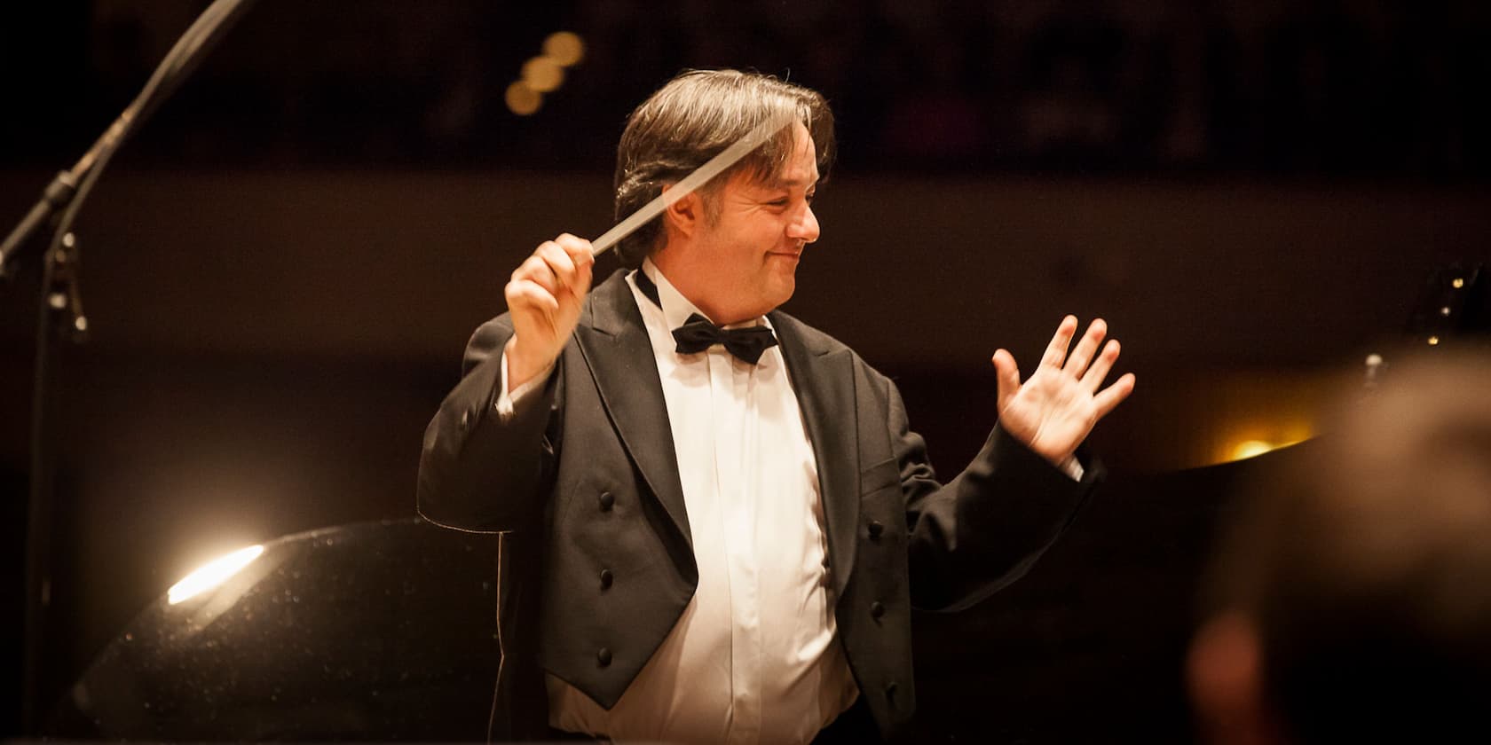 Conductor in a black suit conducting an orchestra.