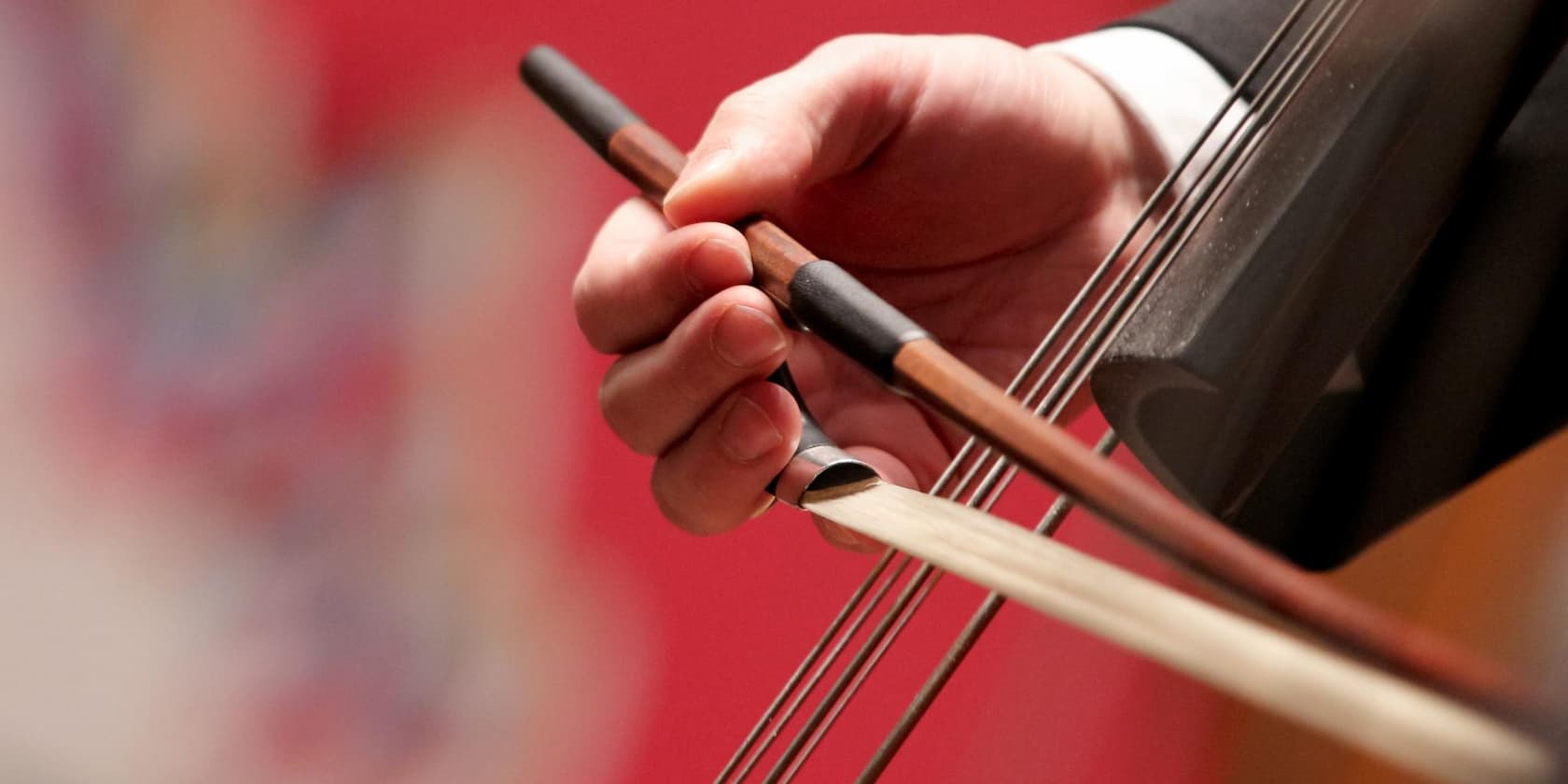 Hand holding a violin bow and playing on strings