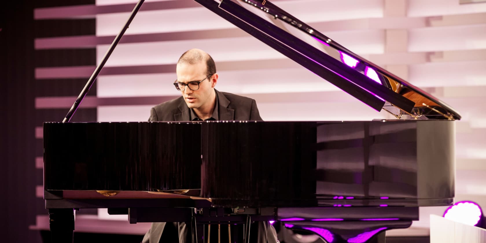 A man plays piano in a modern room with purple lighting.