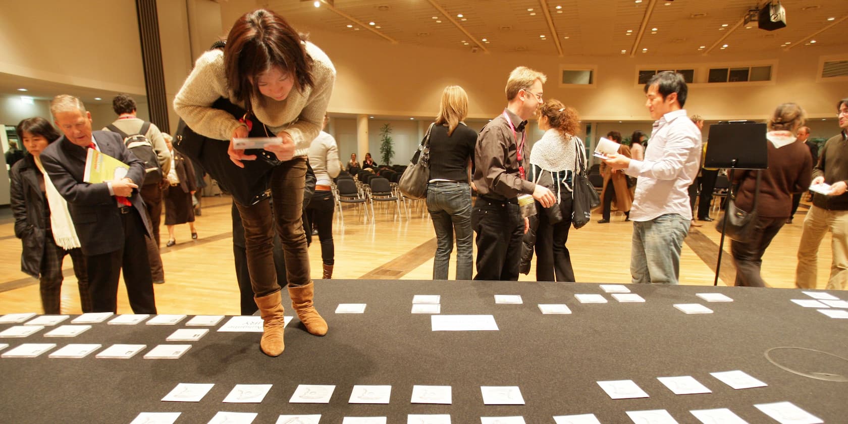 People in an event hall looking at cards on a table.