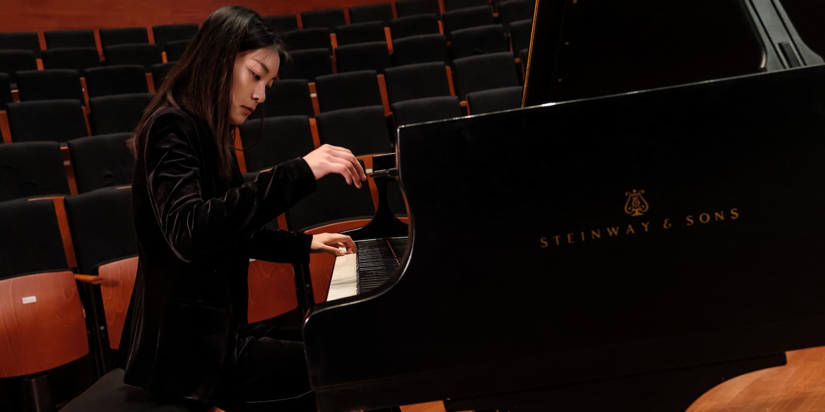 A woman playing piano in an empty concert hall.