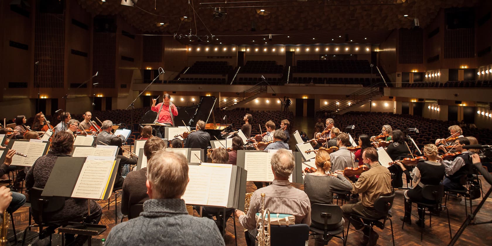 An orchestra rehearses in an empty concert hall, with the conductor standing at the front conducting.