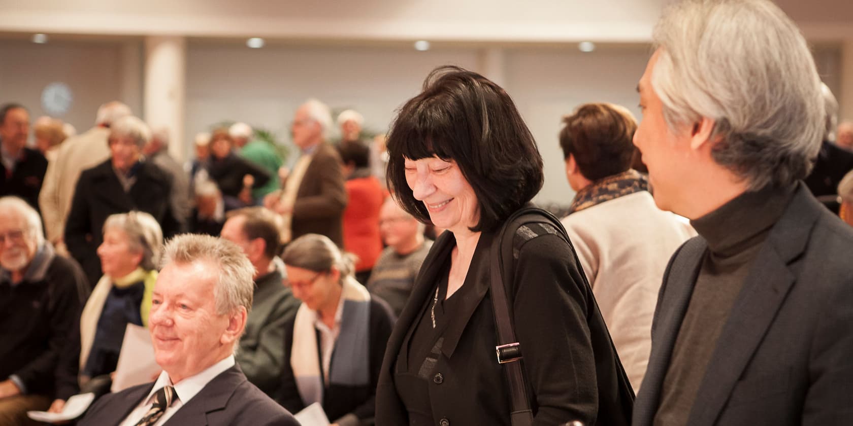 A group of people at a gathering, with a woman in the center smiling.