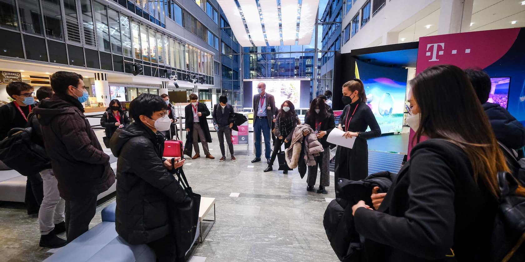 People wearing masks gather in the lobby of a large company.