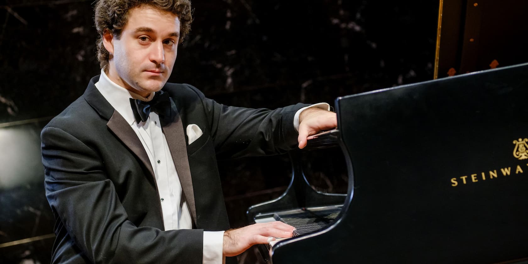 A man in a tuxedo plays a Steinway grand piano.