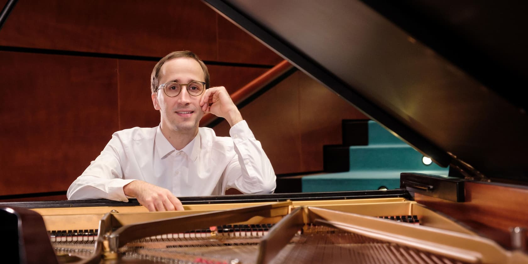 A person in a white shirt sits at an open piano and smiles.