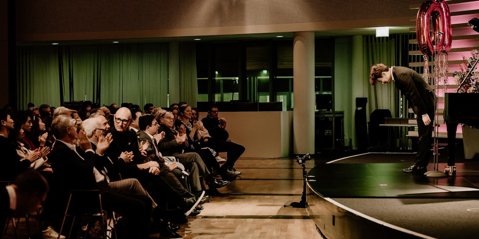 A man in a suit is bowing to an applauding audience in an event hall.