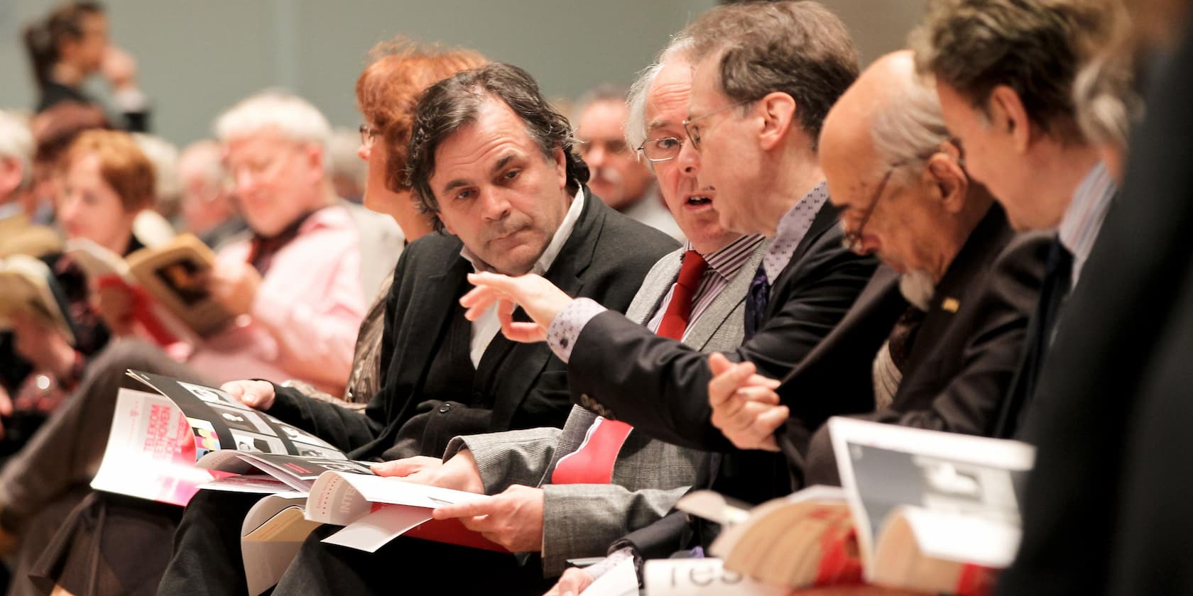 People sitting in a row reading or talking at an event.