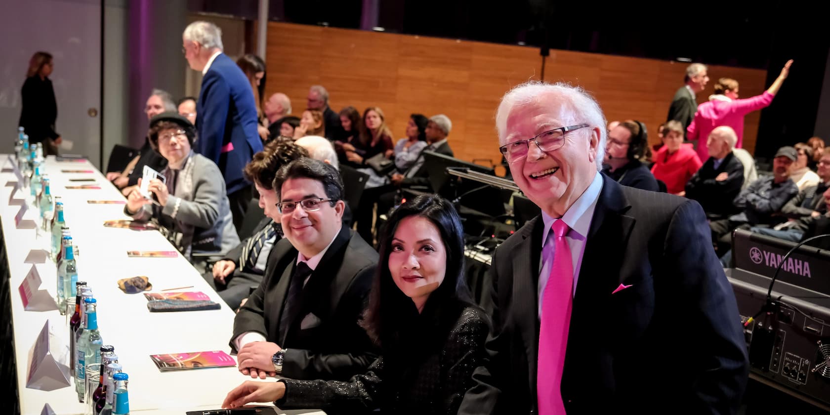 Menschen sitzen an einem langen Tisch in einer Konferenz und lachen.