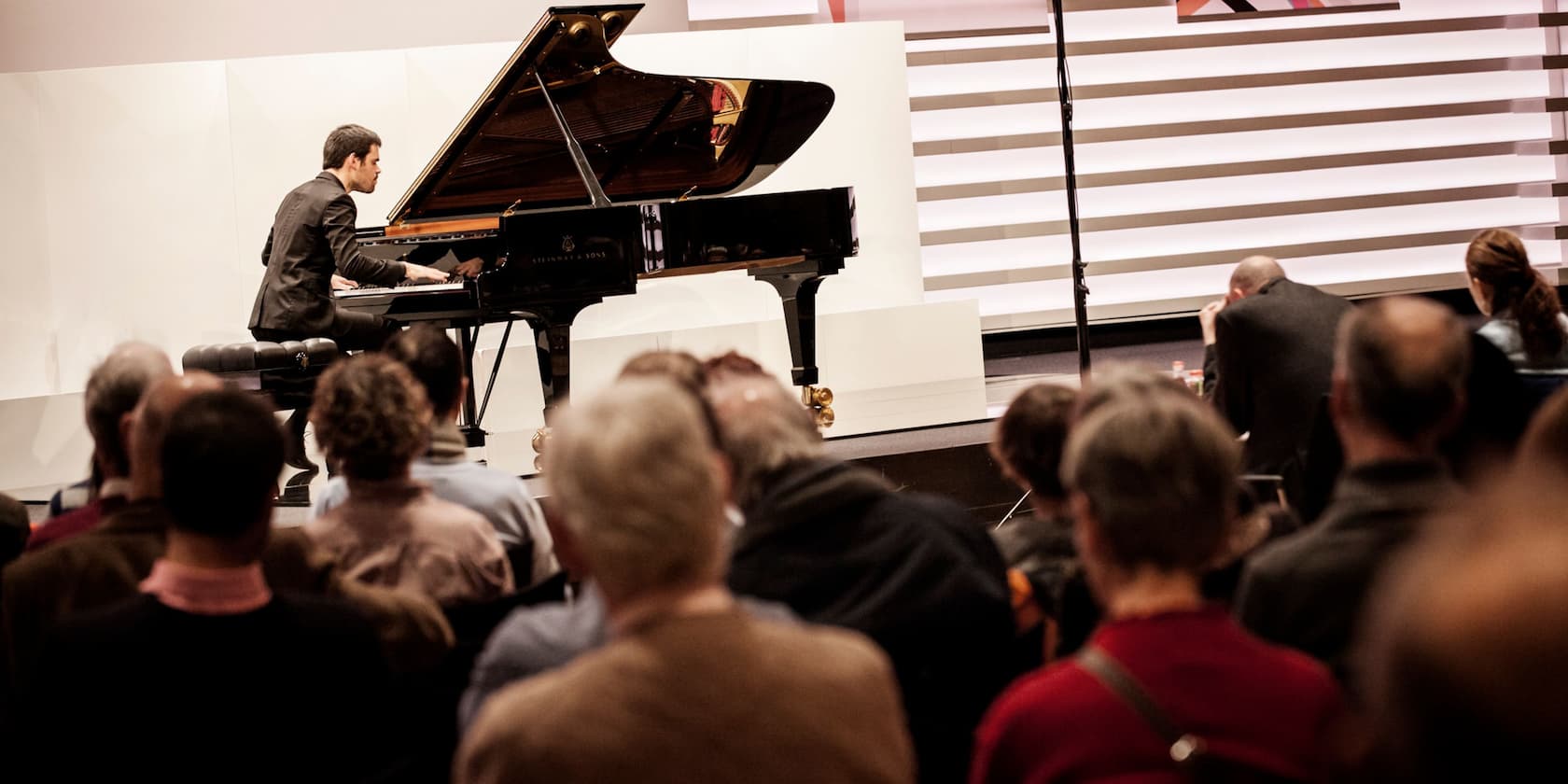 A man plays a grand piano in front of an audience.