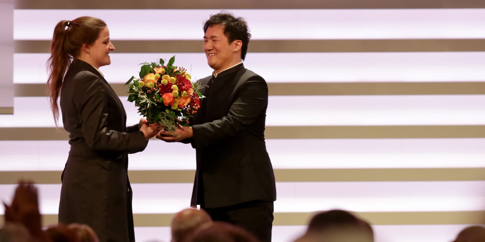 A person hands a bouquet of flowers to another person on a stage.