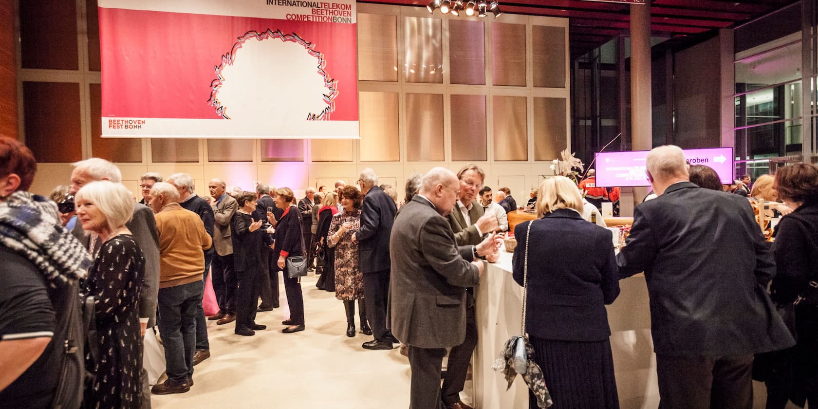 A reception at the Beethoven Competition Bonn, people standing and talking under a large banner.