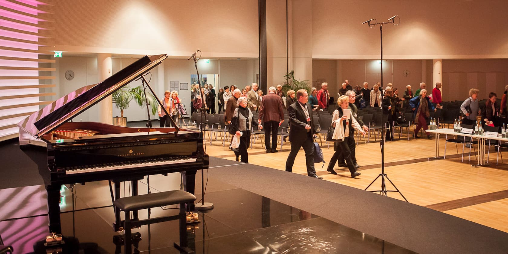 A grand piano and people walking through an event hall.