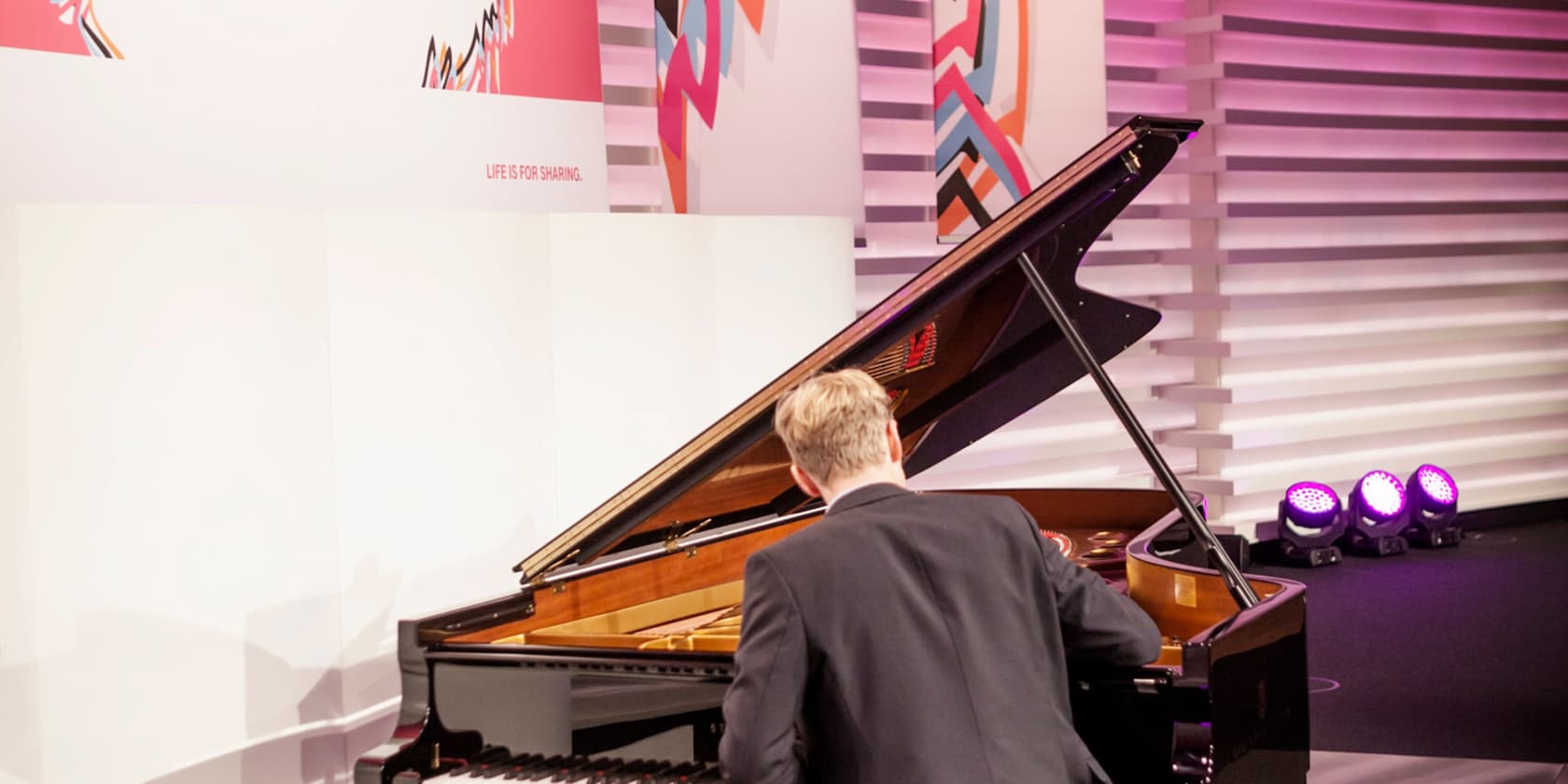 Man playing piano on a stage with modern, colorful patterns in the background.