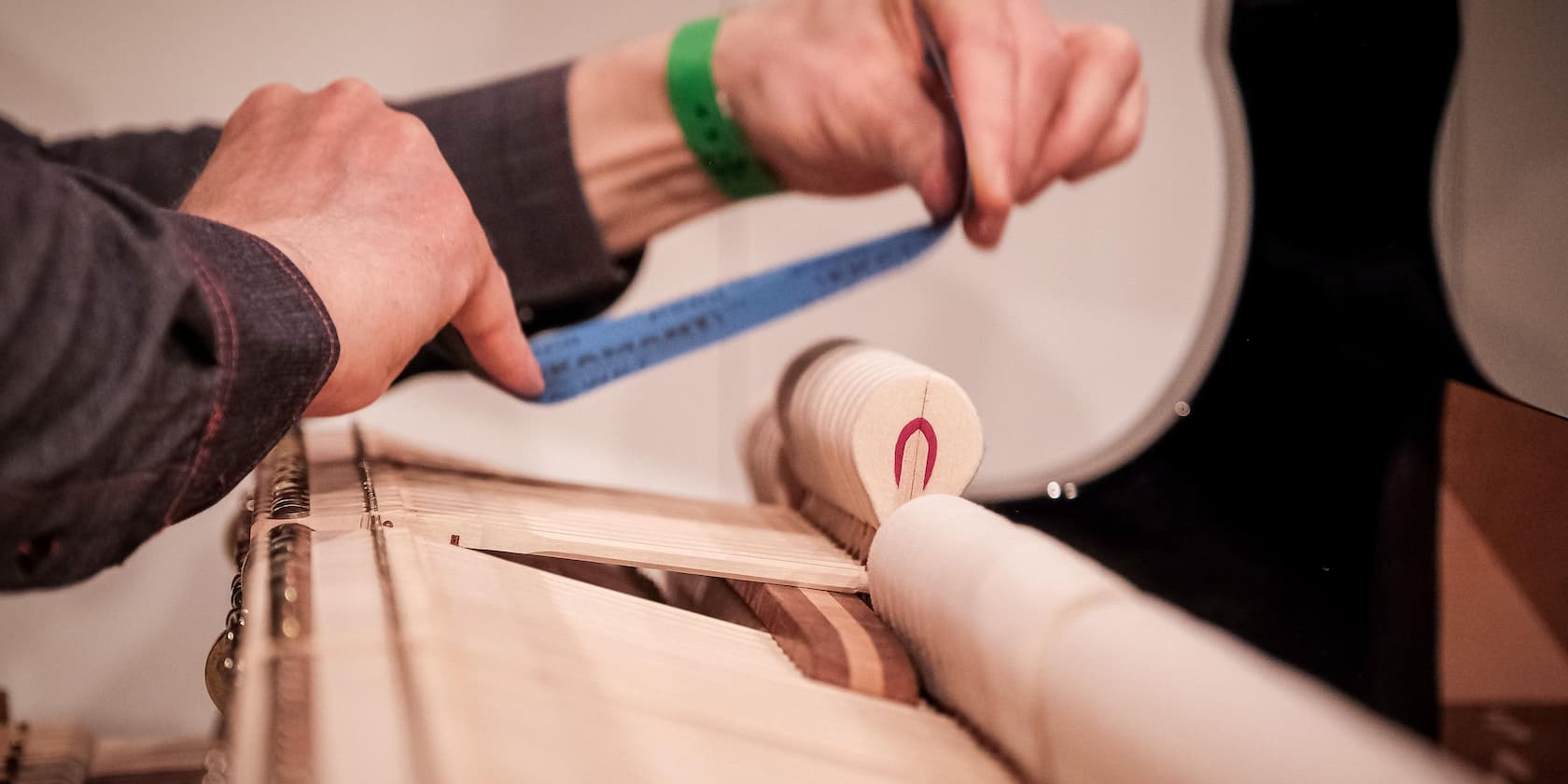 A person measuring with a blue tape measure on a piano mechanism.