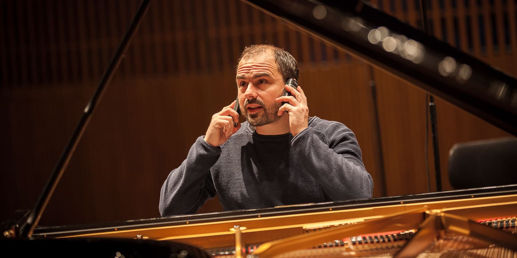 Ein Mann sitzt an einem Klavier und spricht gleichzeitig in zwei Handys.