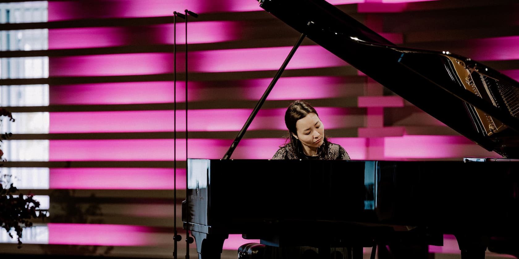 A woman playing piano on a stage with purple backlighting.