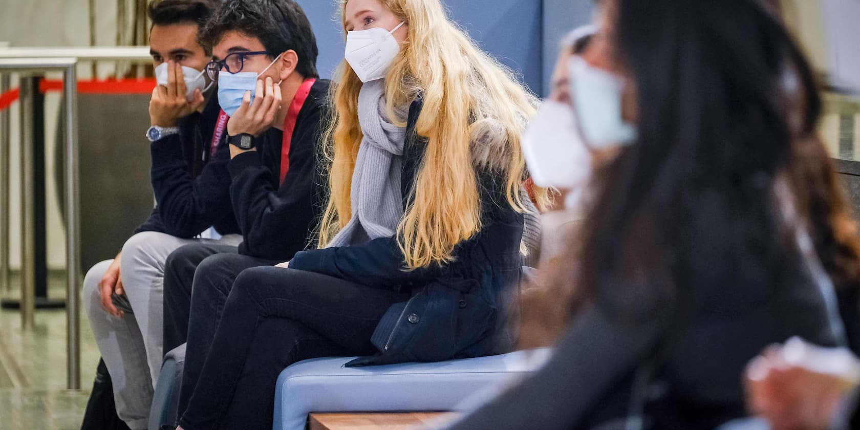 Personen mit Gesichtsmasken sitzen in einer Wartelounge.