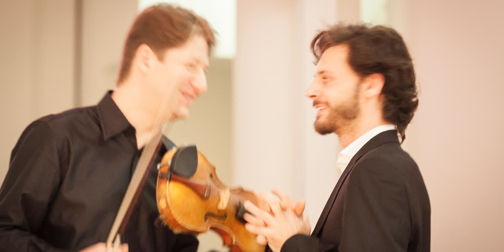 Two men are conversing; one is holding a violin.