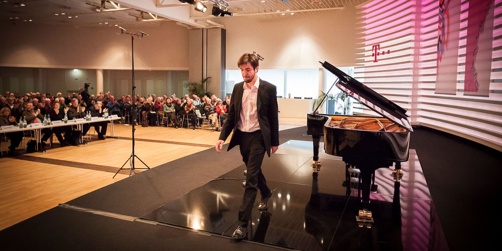 A man leaves the stage after a piano performance. The audience in the background is clapping.