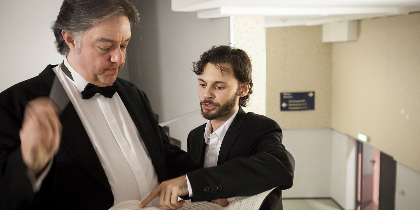 Two men in formal wear looking at a musical score.